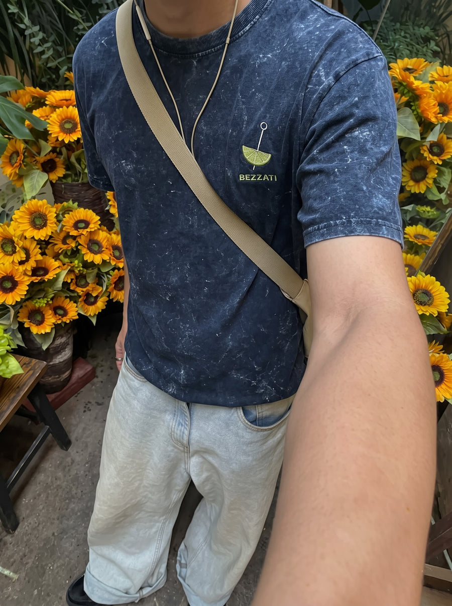 Front of the navy acid-wash t-shirt, a small cocktail mark above the Bezzati wordmark, worn in front of sunflowers