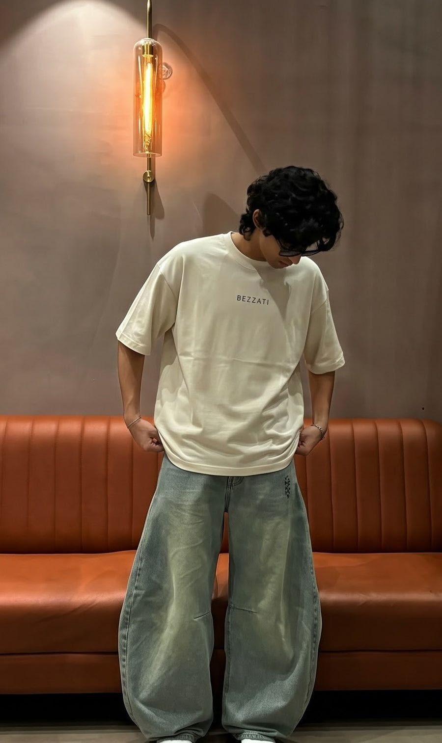 Off-white oversized t-shirt with the Bezzati chest wordmark, worn indoors beside an orange banquette