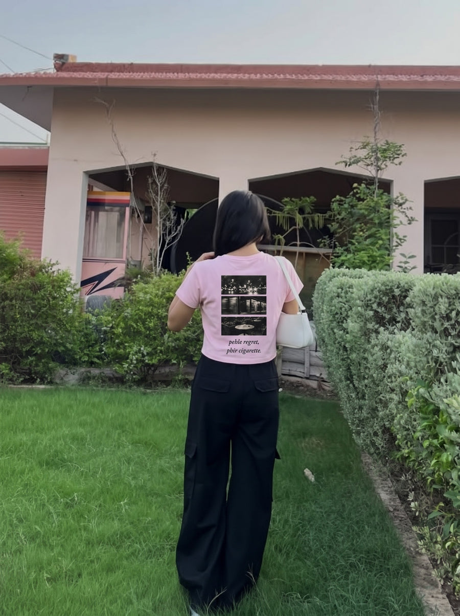 Pehle Regret Phir Cigarette baby tee in light baby pink, worn from behind with black cargo trousers, the night-photo triptych printed across the back