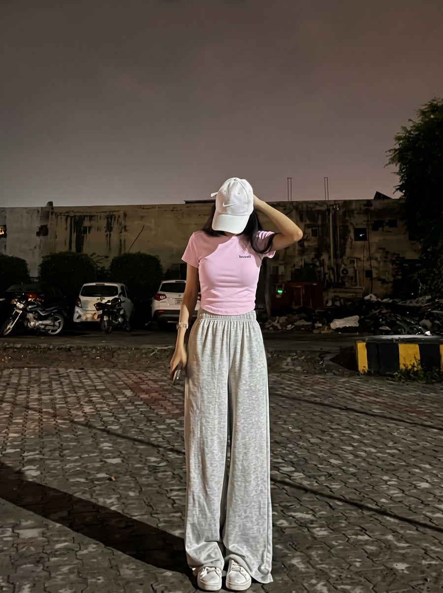 Light baby pink Pehle Regret Phir Cigarette cropped baby tee worn with a white cap and grey wide-leg joggers, small bezzati wordmark on the chest