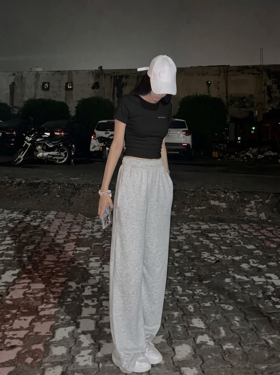 Black Open Waters cropped baby tee worn with a white cap and grey wide-leg joggers, small BEZZATI wordmark on the chest