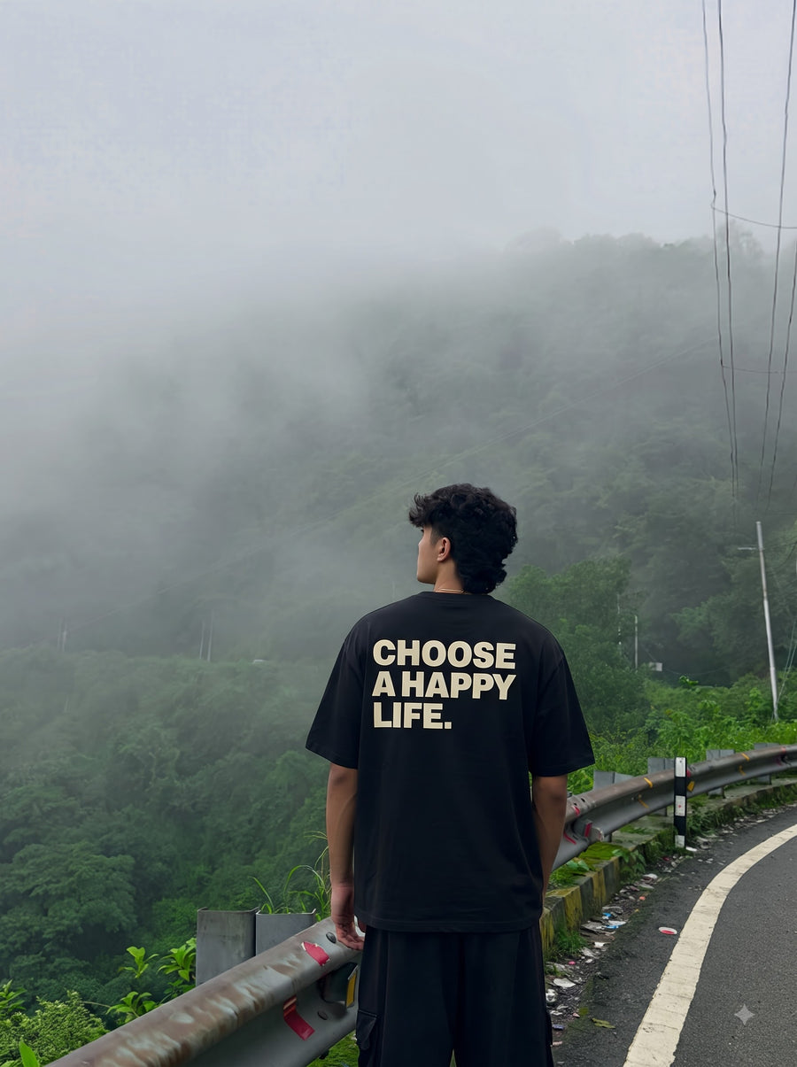 Happy Life oversized t-shirt in Black, worn from behind on a misty hill road, with Choose a happy life in heavy cream capitals across the back