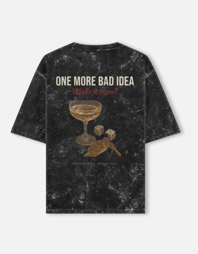 One More Bad Idea back print on a black acid-wash oversized t-shirt, with a coupe glass and a pair of dice below the type