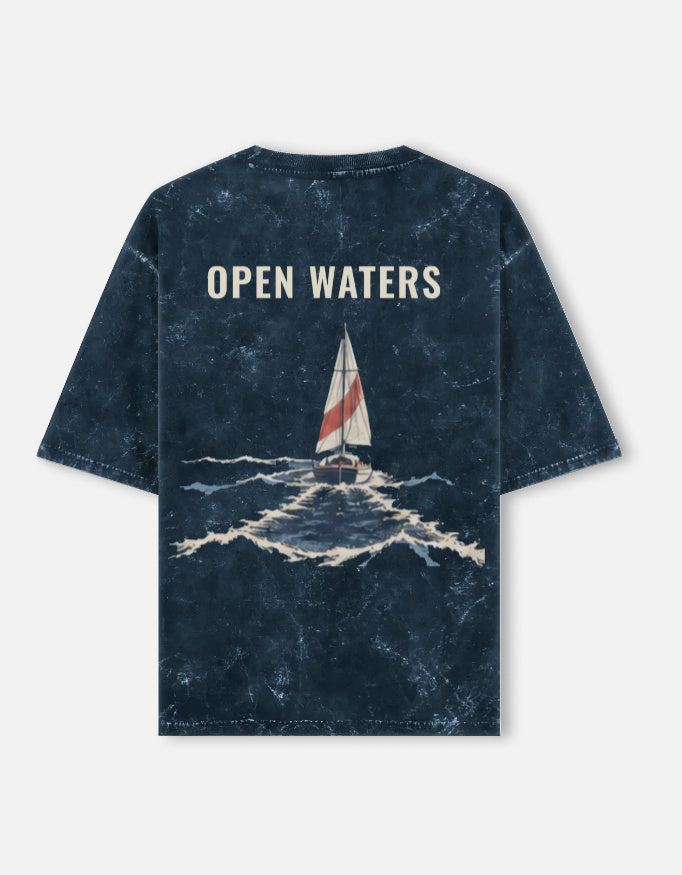Open Waters back print: a boat crossing heavy seas, on a navy acid-wash oversized t-shirt