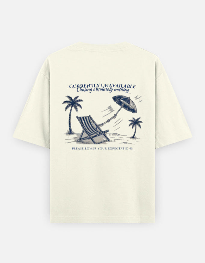 Currently Unavailable back print on an off-white oversized t-shirt, with a deck chair, palm trees and a beach umbrella blowing away