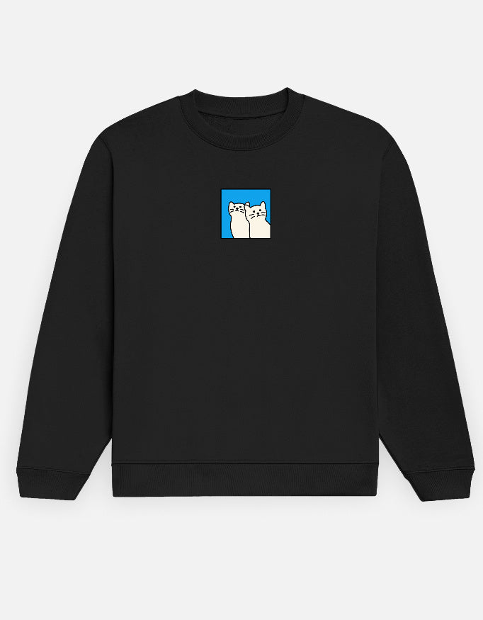 Front of the black Cats unisex sweatshirt: two cream cartoon cats sitting side by side inside a bright blue square, centre chest
