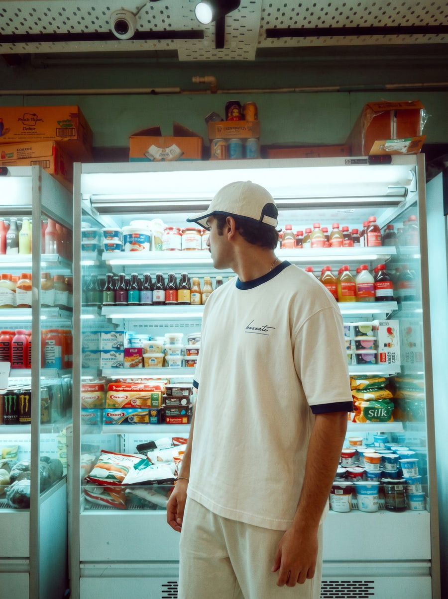 A cream ringer tee with contrast collar and cuffs, worn in front of a lit shop cooler at night.