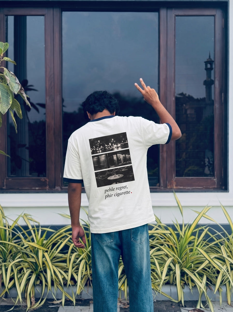 An off-white tee carrying the black-and-white photographic triptych back print, worn by a window in daylight.