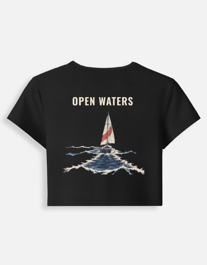 Open Waters baby tee in black, back print of a sailboat with a red-striped sail on breaking waves under the words Open Waters