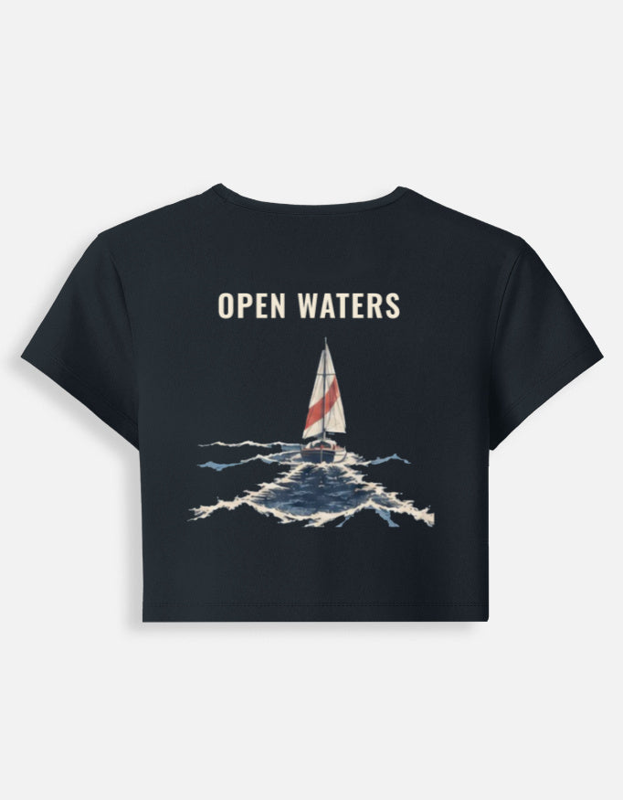 Open Waters baby tee in navy blue, back print of a sailboat with a red-striped sail on breaking waves